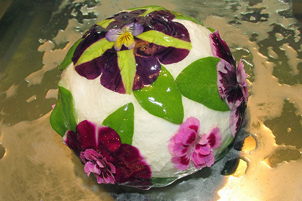 Close up of purple and pink flowers with glaze on them on ball of cheese