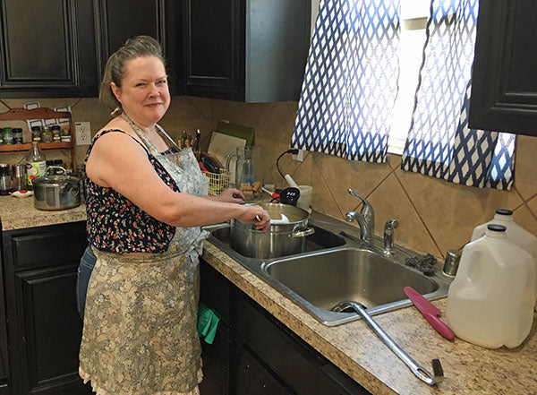 Paula Barnett, cheese maker, smiles for the camear while stirring a pot that sits in a kitchen sink