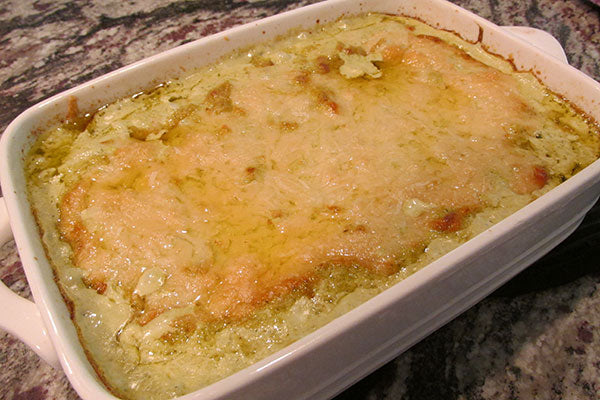 A white ceramic baking dish filled with cheesy baked cauliflower sits on a granite countertop