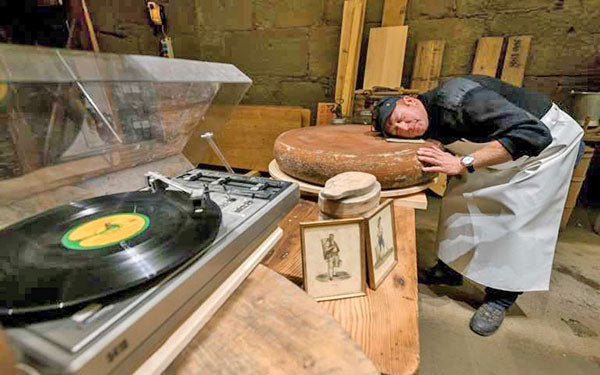 Man laying head on a large circular block of cheese on a table