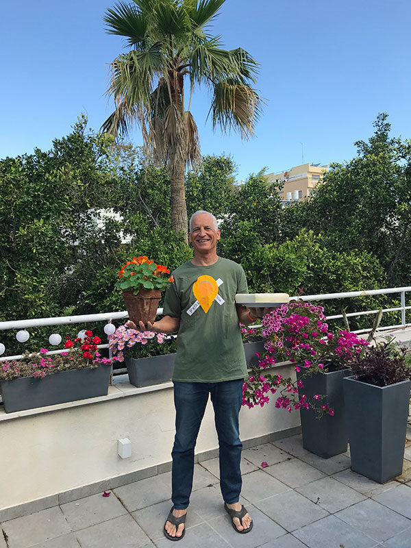 A man smiles while holding a plate of cheese in one hand and a pot of flowers in the other hand